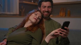 Relaxed happy married family couple Caucasian man woman husband wife hugging rest on sofa home shopping in internet store using mobile application play online game on phone laughing ordering delivery - Powered by Shutterstock - Get 15% off with code: PIKWIZARD15
