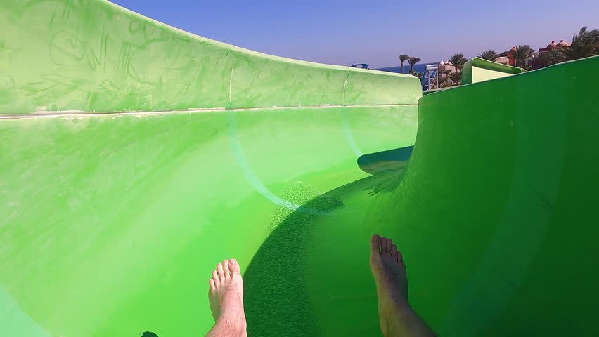 Going down on fast water slide on an inflatable ring in outdoor water park with legs in the frame, pov view