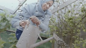 Animation of water drops over biracial woman in hijab with watering can, gardening. Hobby, lifestyle, domestic life and happiness concept digitally generated video.
