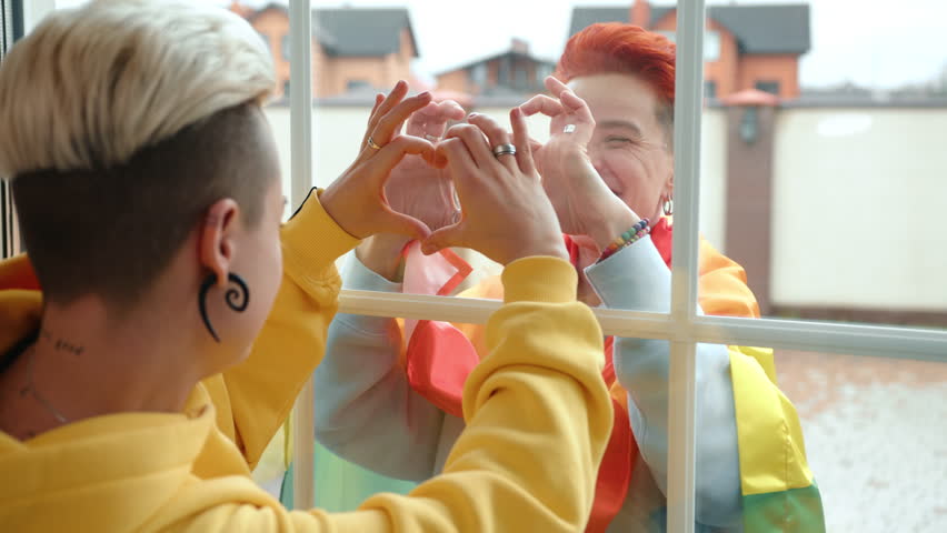 A poignant representation of love and unity as one lesbian woman on the street and her partner indoors form a heart shape through the glass, symbolizing a strong bond. Camera 8K RAW. 