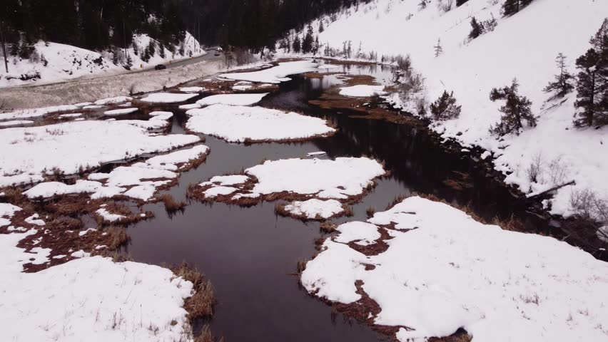 camera moves along the road and snow-covered mountains catching the reflections of the sky in the frozen river.