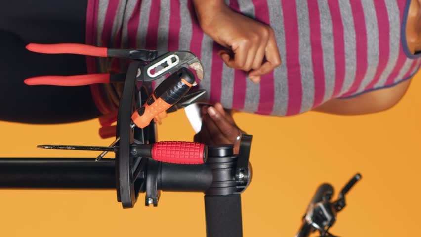 Vertical video African american mechanic utilizing different tools to repair damaged bike handlebar grips, studio background. Employee using specialized gear to fix shifters and brake levers on Royalty-Free Stock Footage #3435449007
