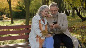 Caucasian retired couple family in love mature woman man sit on bench autumn park using mobile phone gadget together smiling wife husband spouses reading news old age and smartphone in city outdoors - Powered by Shutterstock - Get 15% off with code: PIKWIZARD15