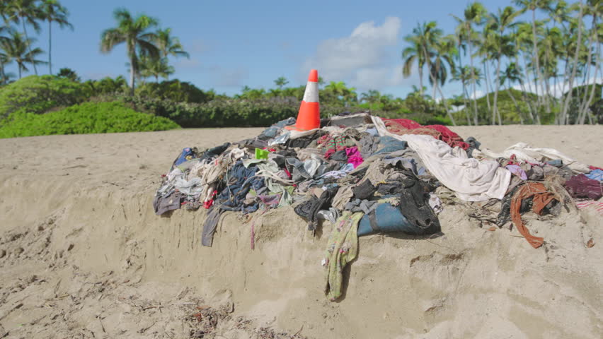 A stack of dirty sandy shore environmental pollution ecological problem, clothes and a traffic cone on a sandy beach with scenic views of the sky clouds and palm trees plants in Oahu Hawaii  Royalty-Free Stock Footage #3435506037