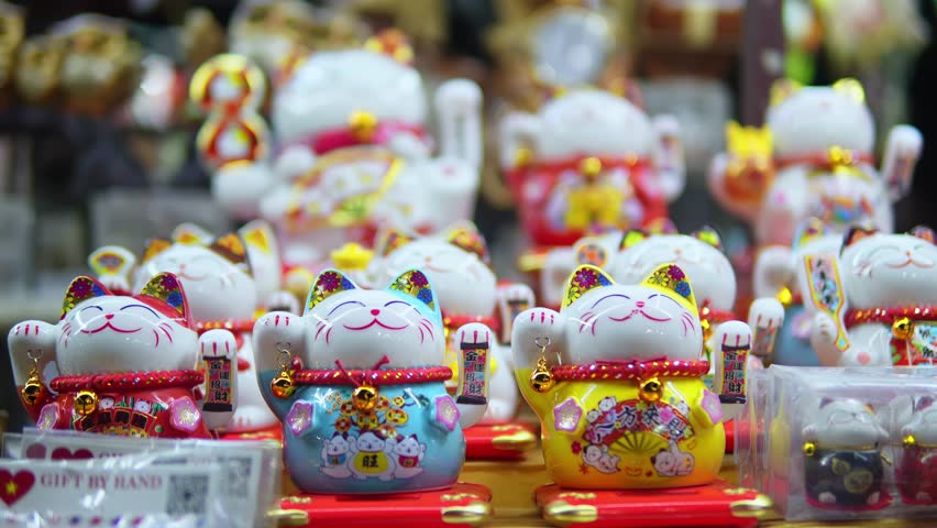 Storefront with variety of traditional Chinese souvenirs in form of cat with moving paw filmed in closeup. Lots of Maneki Neko funny statues usually bought as souvenirs are put in a row on shop window Royalty-Free Stock Footage #3435527331