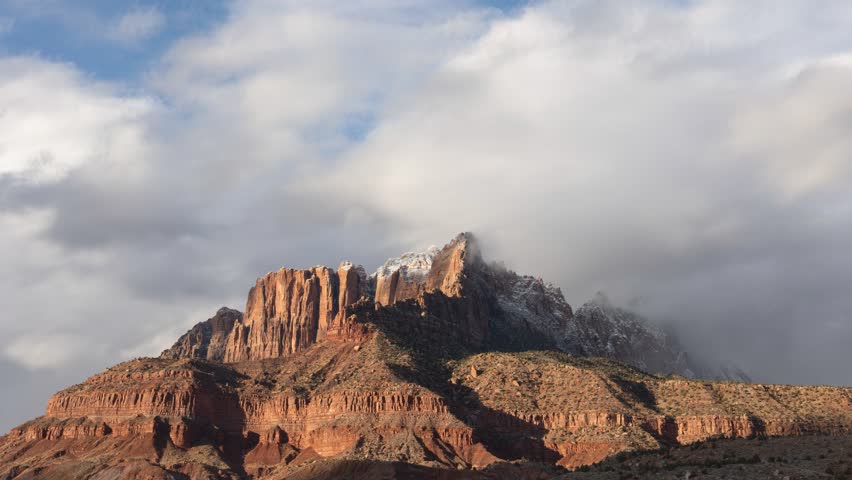 4k time lapse video of low winter clouds drifting over Mt. Kinesava in Zion Nat. Park, Utah, USA as sun gradually sets painting the cliffs brilliant orange and the clouds pink before fading to blue