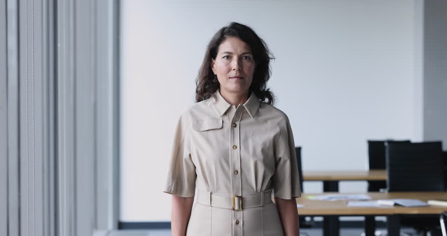Serious mature business leader woman posing in office space, looking at camera, getting happy, cheerful, laughing, putting hands into pockets. Positive confident businesswoman, entrepreneur portrait