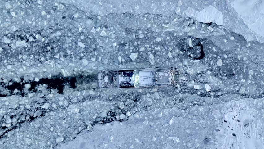 A small icebreaker clears a path through the ice for other ships. View from above.