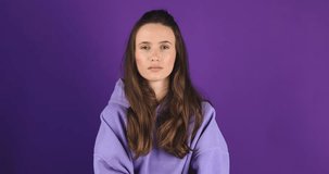 Smiling attractive brunette woman looking at camera listening to someone and nodding with agree standing over purple violet studio background. Girl wave her head.