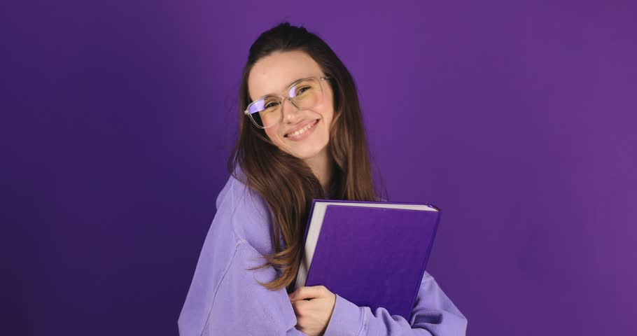 Brunette woman student holding book with happy expression over isolated purple background. Girl wear glasses smiling and hold book. Love reading concept. Royalty-Free Stock Footage #3435641853