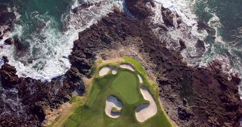Drone video of waves hitting the rocks on the seashore next to a beautiful golf course