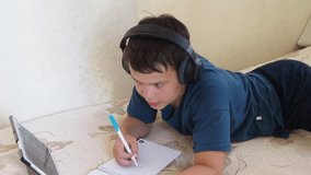 Portrait of a boy using tablet computer and headphone during pandemic lockdown, homeschooling, social distance, stay at home, online education concept. teenager doing homework using a computer.