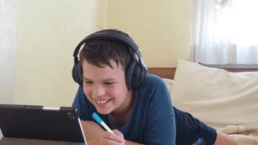 Portrait of a boy using tablet computer and headphone during pandemic lockdown, homeschooling, social distance, stay at home, online education concept. teenager doing homework using a computer.