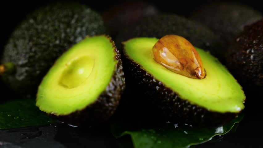 Drops of water fall on avocado fruits with leaves on a black background. Raw Fruits, healthy food.