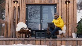 Mature man working from cozy cabin in mountains, sitting on terrace with laptop, enjoying cup of coffee. Concept of remote work from beautiful, peaceful location. Hygge at work. - Powered by Shutterstock - Get 15% off with code: PIKWIZARD15