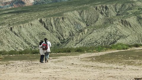 Two Female Primary School Student Friends walk hugging each other Toward the Mountains in the Altiplano, Salta Province, Argentina, South America.  