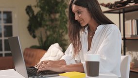 A young girl is sitting at a computer working from home. Freelancer is a young woman beautiful and stylish