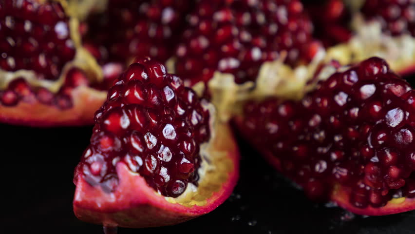 Rotating red pomegranate cross section on black background. Drops of water fall on pomegranate grains.