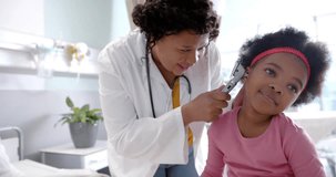 Animation of dna strands over african american female doctor checking ear of happy girl patient. Digital interface, connection, hospital and healthcare, digitally generated video.