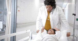 Animation of dna strands over african american female doctor pushing girl patient in hospital bed. Digital interface, connection, hospital and healthcare, digitally generated video.