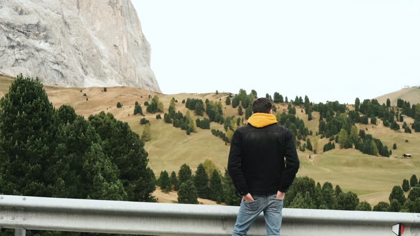 Hiker standing on top of a mountain peak looking at snowy Italian Alps