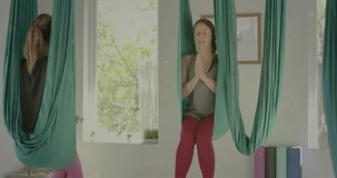 Animation of green lights over caucasian female aerial yoga instructor and teenage girl meditating. Wellbeing, energy, relaxation and healthy lifestyle, digitally generated video.