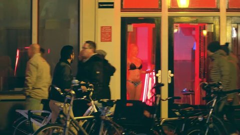 AMSTERDAM, NETHERLANDS - DECEMBER 27, 2017. Tourists walk by prostitutes windows in famous red light district De Wallen