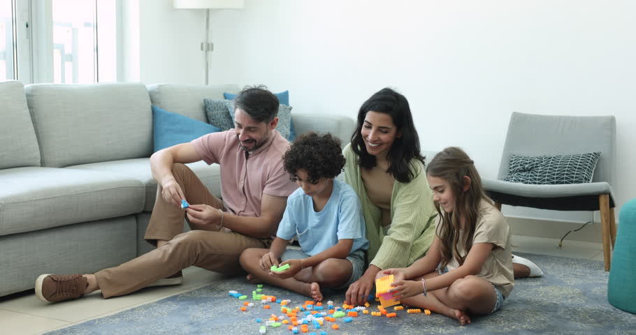 Multinational family spend time together play plastic building blocks. Multiracial spouses and little cute children enjoy pastime and playtime and communication seated on floor in modern living room Royalty-Free Stock Footage #3436140131