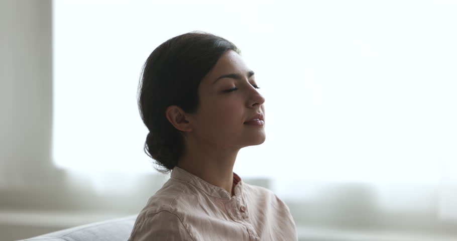 Indian woman resting on sofa with eyes closed do meditation, deep relaxation practice, enjoy pleasant fragrance, humidifier or scented fresh conditioned air inside living room feel serenity, close up Royalty-Free Stock Footage #3436144299