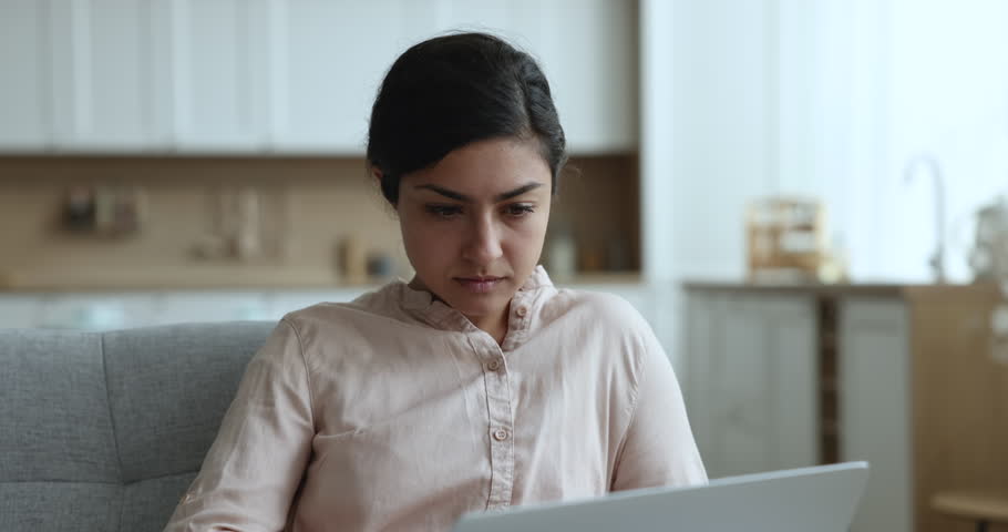 Indian young woman sit on sofa at home work on laptop distantly, feel desperate have unexpected device malfunction, read bad e-mail news, unsaved important information, angry due no internet access Royalty-Free Stock Footage #3436145037