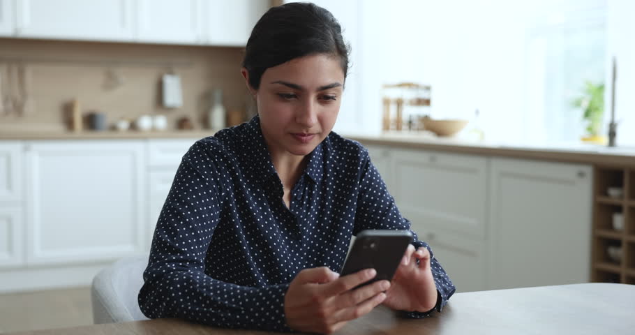 Young Indian woman sit at kitchen hold mobile phone, received awful news feels nervous and indignant, read sms bank notice, experience problem with gadget due low battery, no wi-fi signal, apps crash Royalty-Free Stock Footage #3436152209