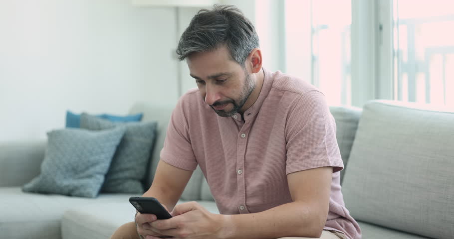 Middle-aged handsome man using cell phone on leisure at home. Millennial generation male spend time on internet, chatting, share messages, search information, single guy using e-dating services app Royalty-Free Stock Footage #3436168765