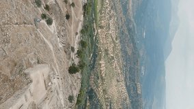 Vertical video. Mycenae, Greece. Excavation site: Greek settlement of the 12th century BC. e. with the ruins of the acropolis, palace and tombs, Aerial View