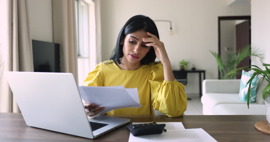 Desperate young Indian woman makes expenses and personal earnings analysis feels disappointed looks desperate, experiences lack of money to pay taxes and bills. Overspending, debt, financial troubles