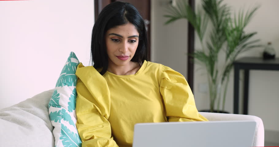 Peaceful young Indian woman sits on couch with laptop, make freelance job, working on project at home, communicate with friends, shopping online in webstore, typing message. Telework, hobby, pastime Royalty-Free Stock Footage #3436237133