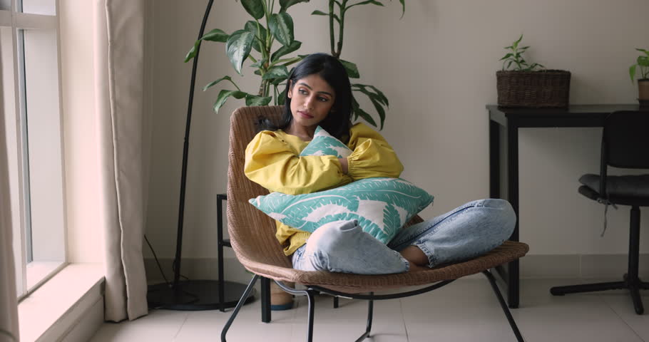 Indian woman looks frustrated or offended cuddling cushion sit in armchair, deep in sad thoughts, missing, waiting, feels bored on a day off at home alone. Loneliness, break up, after quarrel emotions Royalty-Free Stock Footage #3436261085