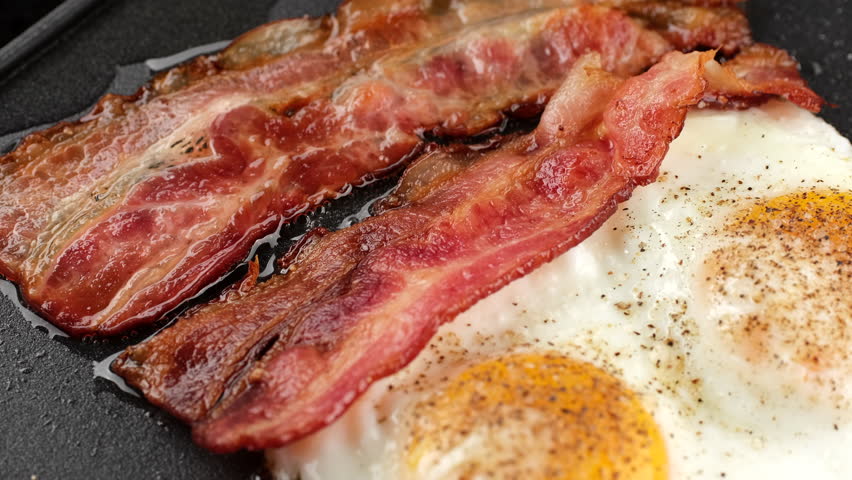 Breakfast with eggs and bacon on grill. Cooking bacon and eggs on pan, slider shot