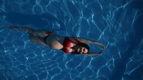 Top view of pregnant woman floating in pool in red bikini. Slow motion. Vertical video. 