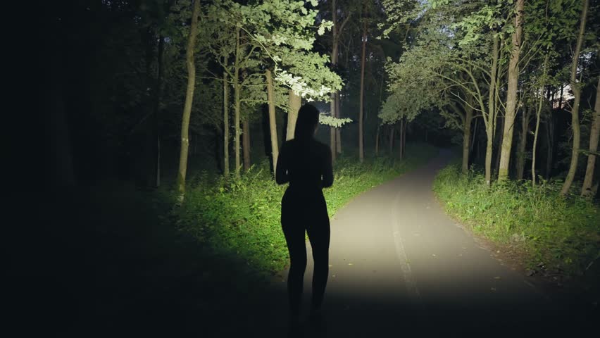 Night running in the park. A bigus woman with a beautiful figure runs along the road at night. Silhouette of an athlete.