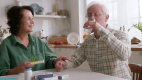 elderly man and woman sit at table in kitchen in morning. takes pills and wash dawn with water. wife supports and cares her husband health. looks kindly and gently smiles, reminding of medications - Powered by Shutterstock - Get 15% off with code: PIKWIZARD15