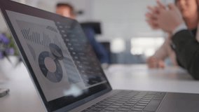 Business report statistics on laptop screen in meeting room close up selective focus. Data graphs on computer with company team talking in blurred background - Powered by Shutterstock - Get 15% off with code: PIKWIZARD15