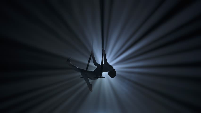 Female gymnast isolated on black background spotlight and smoke. Girl aerial dancer showing acrobatic element on trapeze with straps.