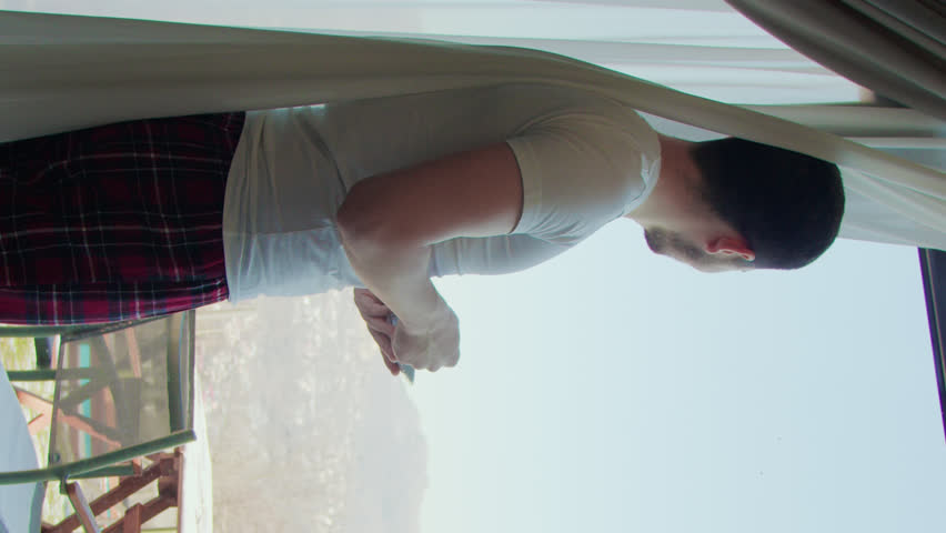 Vertical video in private house man morning tranquility looking panoramic windows bedroom coffee in hand. Serene morning tranquility panoramic windows embodying essence of morning tranquility.