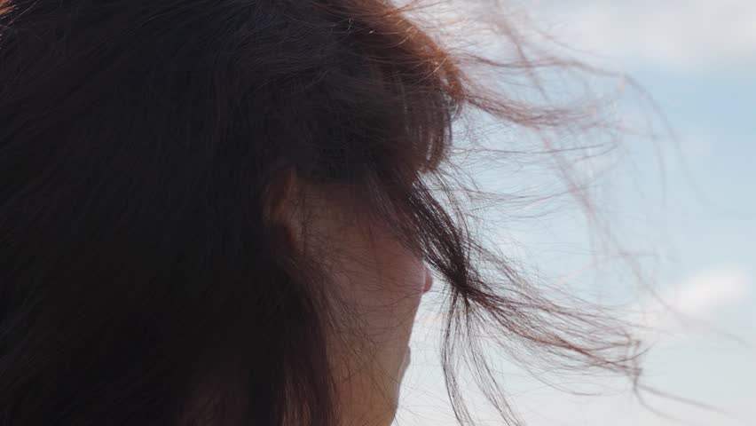 Young woman traveler looks at sky, prays, close-up. Woman dreams, portrait of girl. Girls hair fluttering in wind, adventure, nature tourism. Beautiful flowing female brown hair. Faith in God prayer