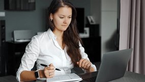 Young woman using laptop in home workplace, writing notes, female student learning and watching online webinar or listening audio course, e-learning education concept. High quality 4k footage