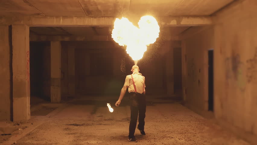 Fire show artist breathe fire in the dark at abandon building, slow motion. Fire in heart shape.
