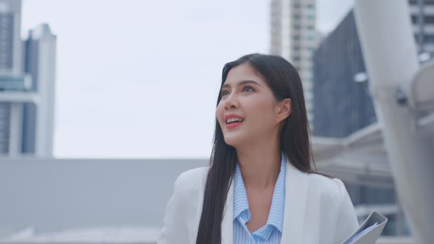Asian youg beautiful businesswoman standing outdoor in modern city. Attractive employee girl worker feel happy and confident walking around outside the office. Job application and recruitment concept.