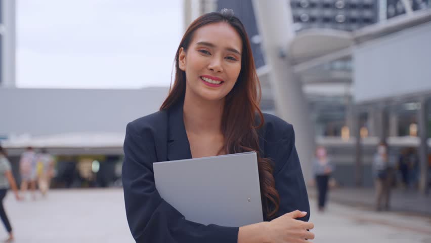 Portrait of Asian youg beautiful businesswoman standing outdoor in city. Attractive employee girl worker feel happy and confident then smile, looking at camera. Job application and recruitment concept