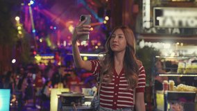 Asian young woman traveler having party and video call on phone in bar. Attractive young girl tourist doing virtual call on smartphone while travel on holiday vacation trip in the city in night club.