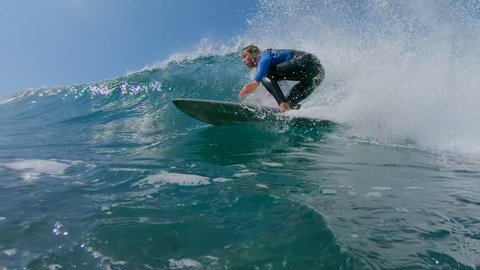 SLOW MOTION, LOW ANGLE, UNDERWATER: Young man surfing a big crashing ocean wave in sunny nature. Surfer carving awesome wave on his cool surfboard. Fit surfer guy riding waves in popular surf spot.